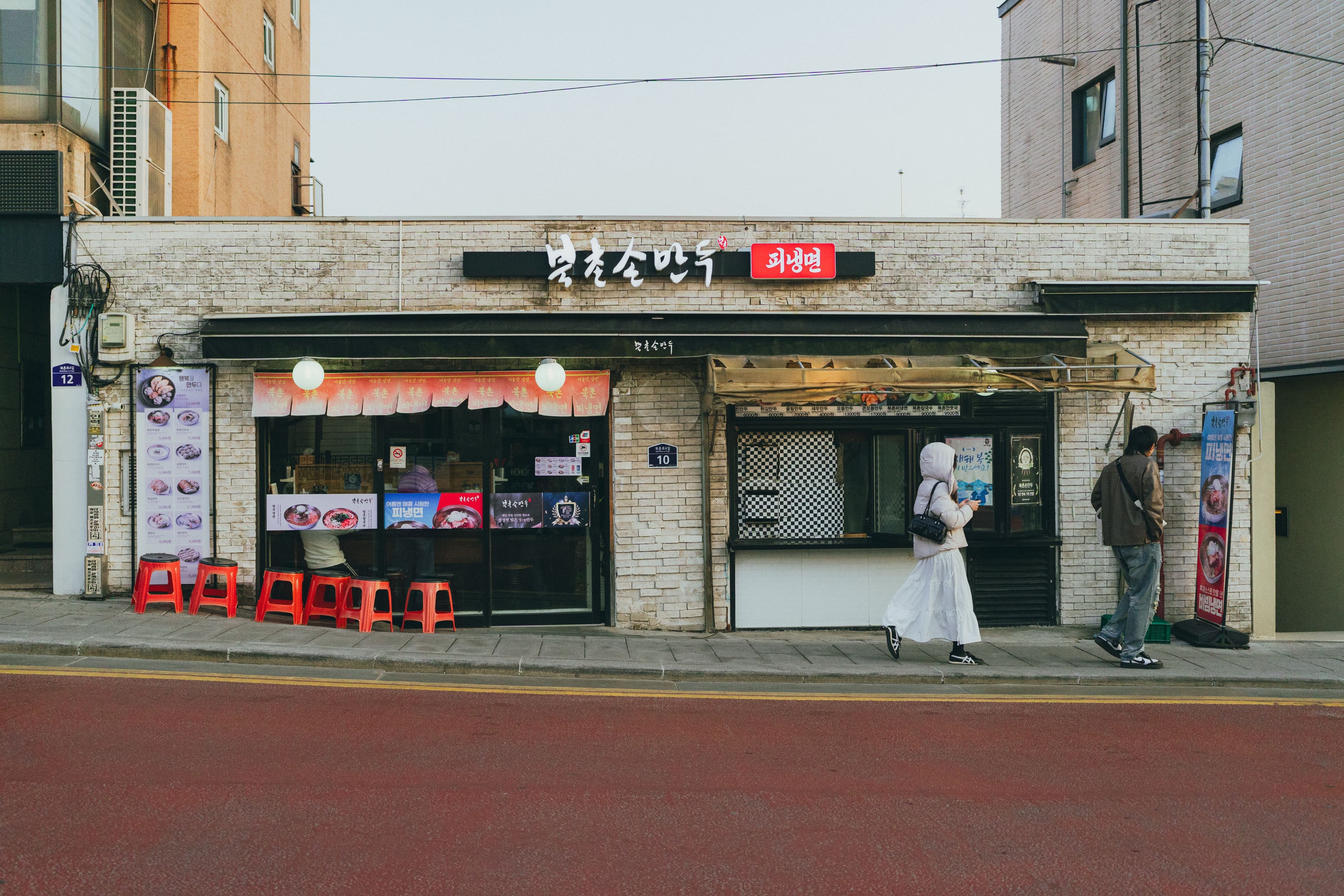 A small independent mandu and naengmyeon shop on a quiet Seoul street, its counter visible through the window